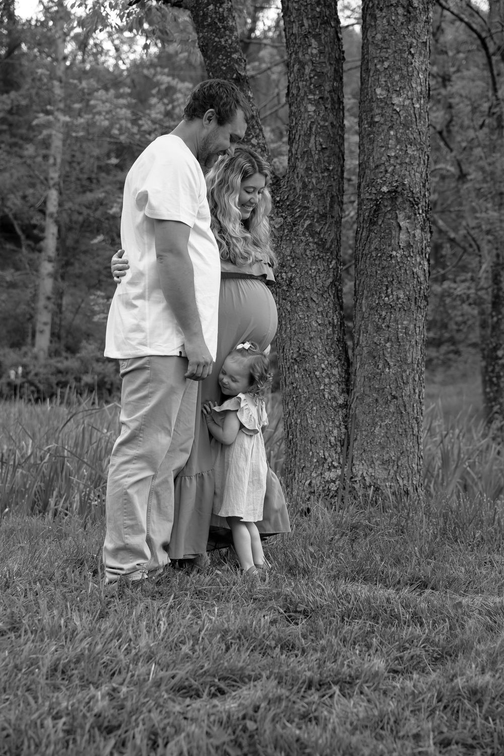 Two people in white and dark clothing stand beside trees in a black and white forest scene.