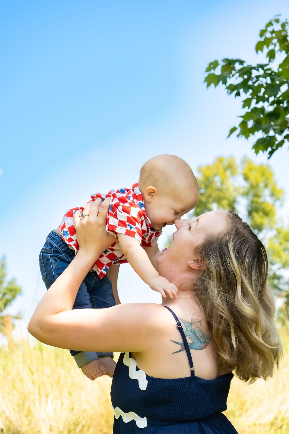 A joyful moment captured between parent and baby against a bright blue summer sky.