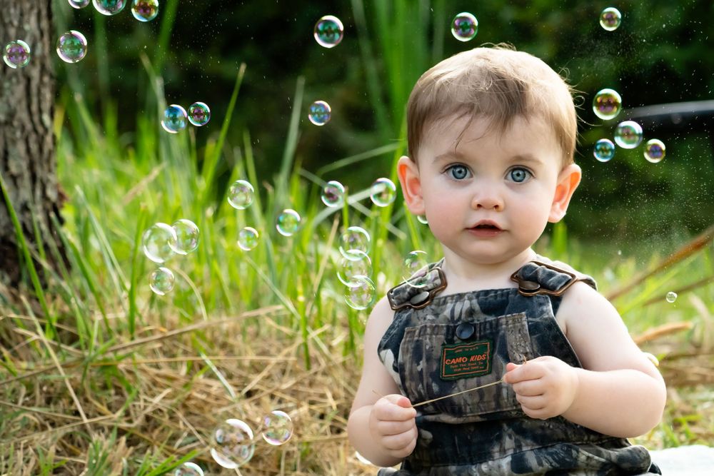 Outdoor portrait with floating bubbles near tree trunk and green foliage.