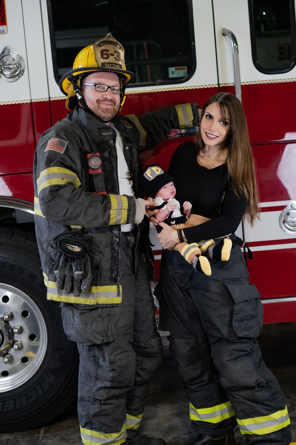 Firefighter in protective gear poses with others beside red fire engine.