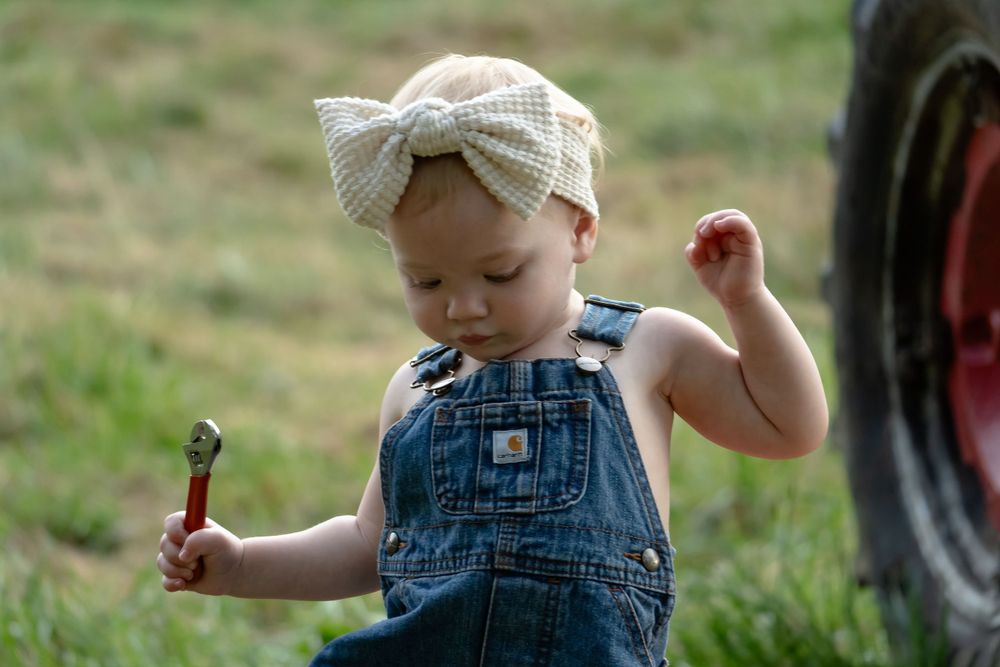 Child wearing denim overalls and knit hat exploring vintage farm equipment.