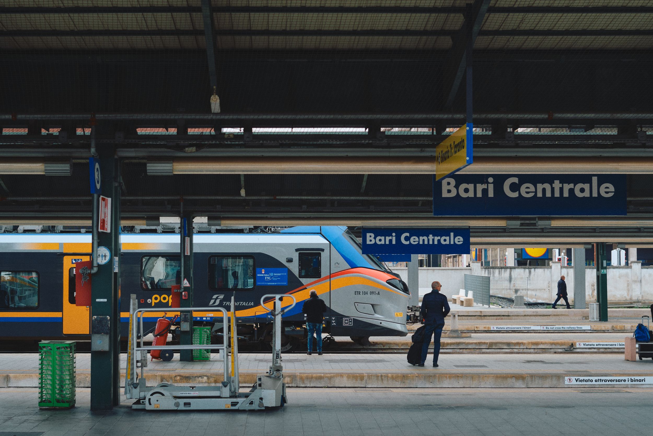 Modern train platform with luggage cart at Bari Centrale station under industrial ceiling.