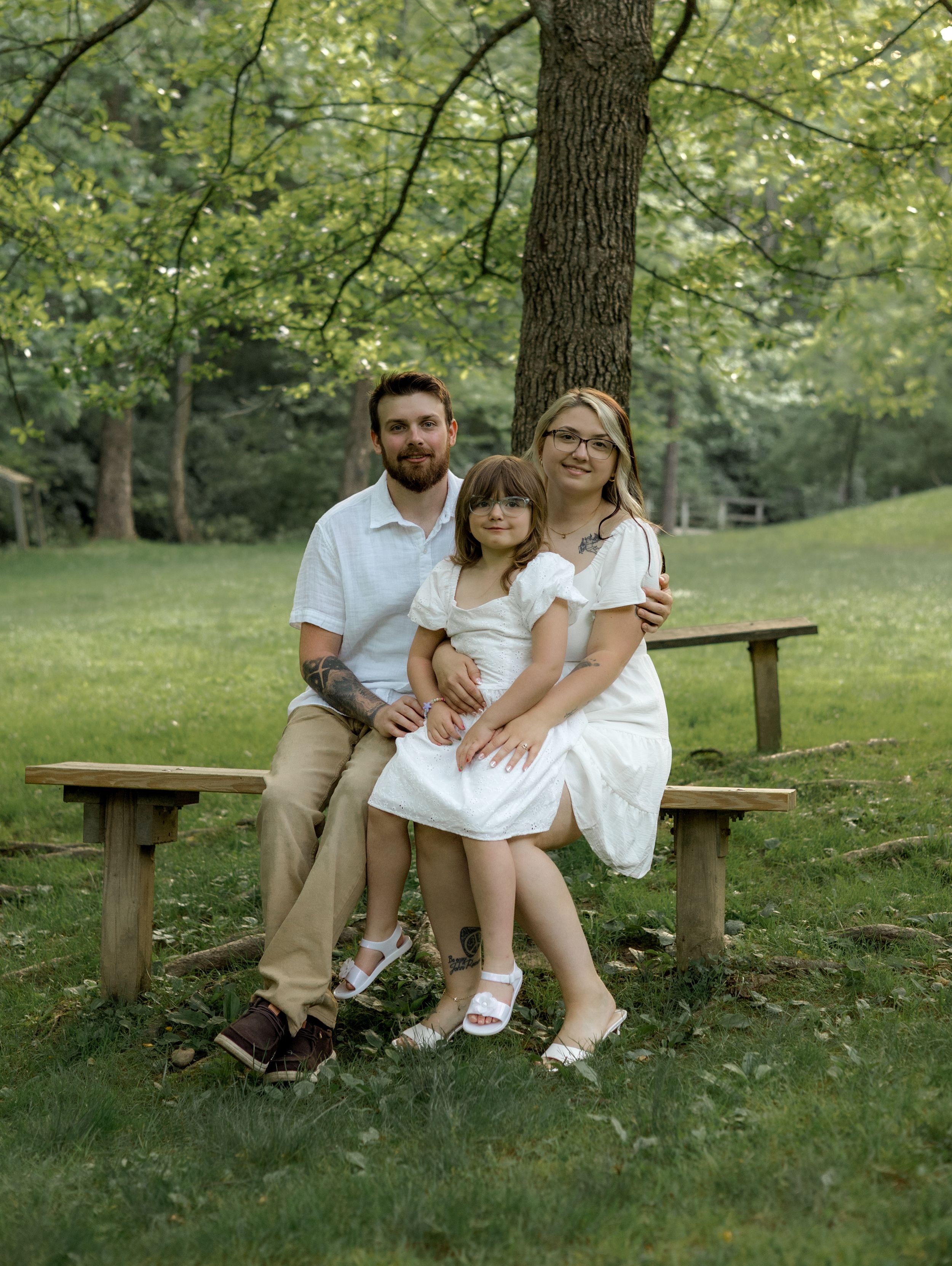 A couple sitting together on a wooden bench in a lush green park setting in casual summer attire.