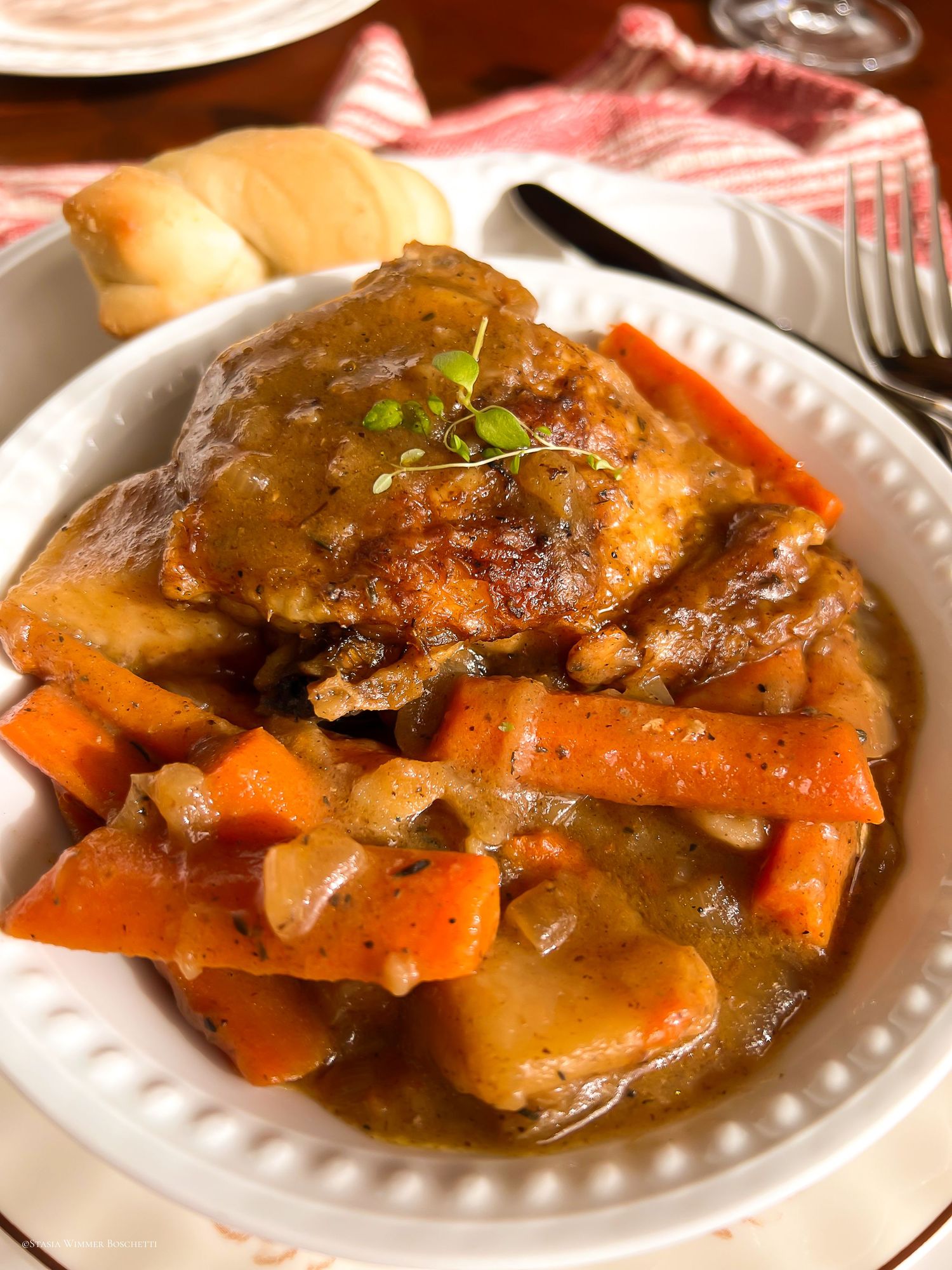 Tender braised meat with carrots and onions in savory sauce on white plates.
