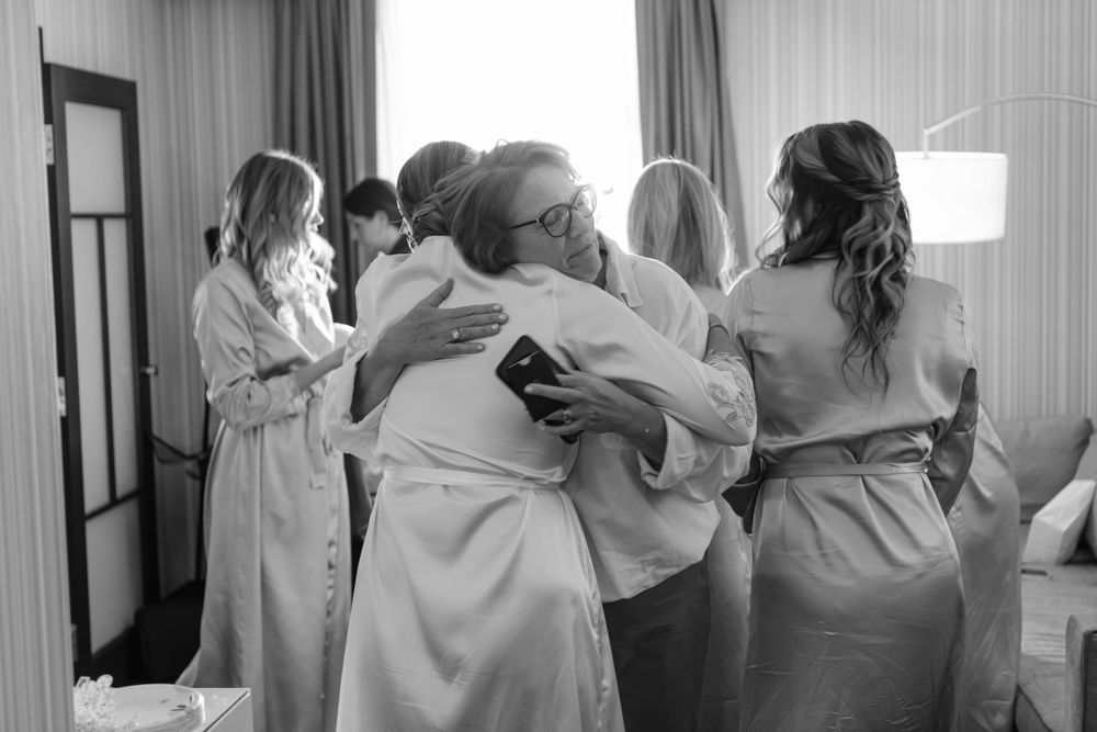 A group in matching robes share an emotional embrace in a bright hotel room before a special event.