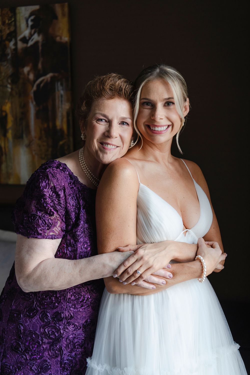 A tender moment shared between a bride and her mother one in a purple lace dress and one in a white wedding gown.