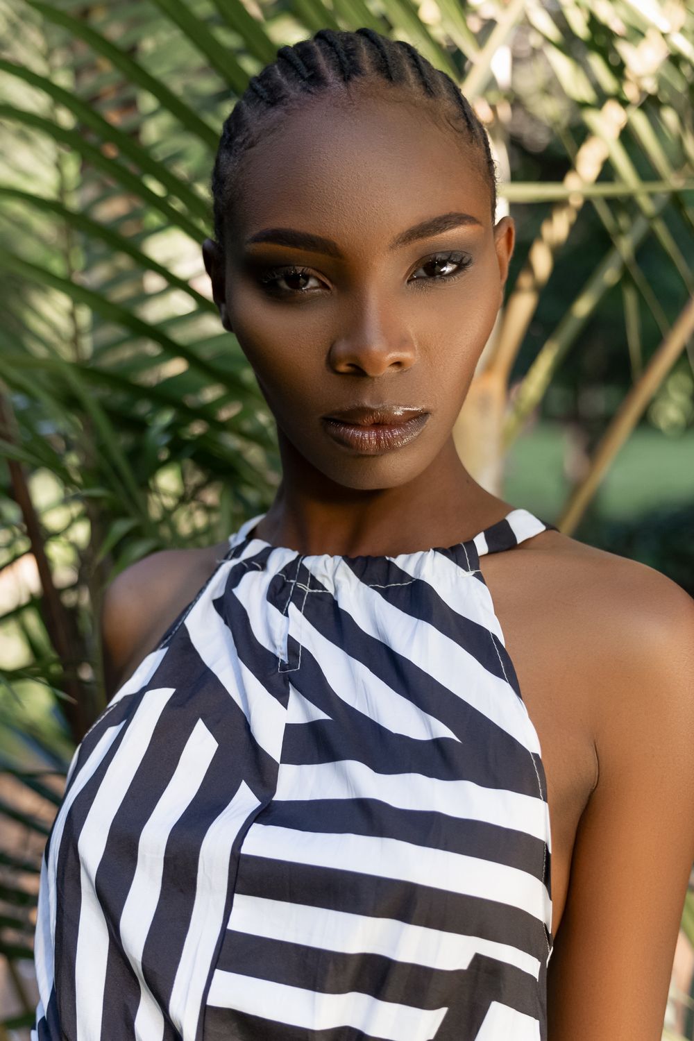 Close up fashion portrait with black and white striped halter top against tropical foliage background.