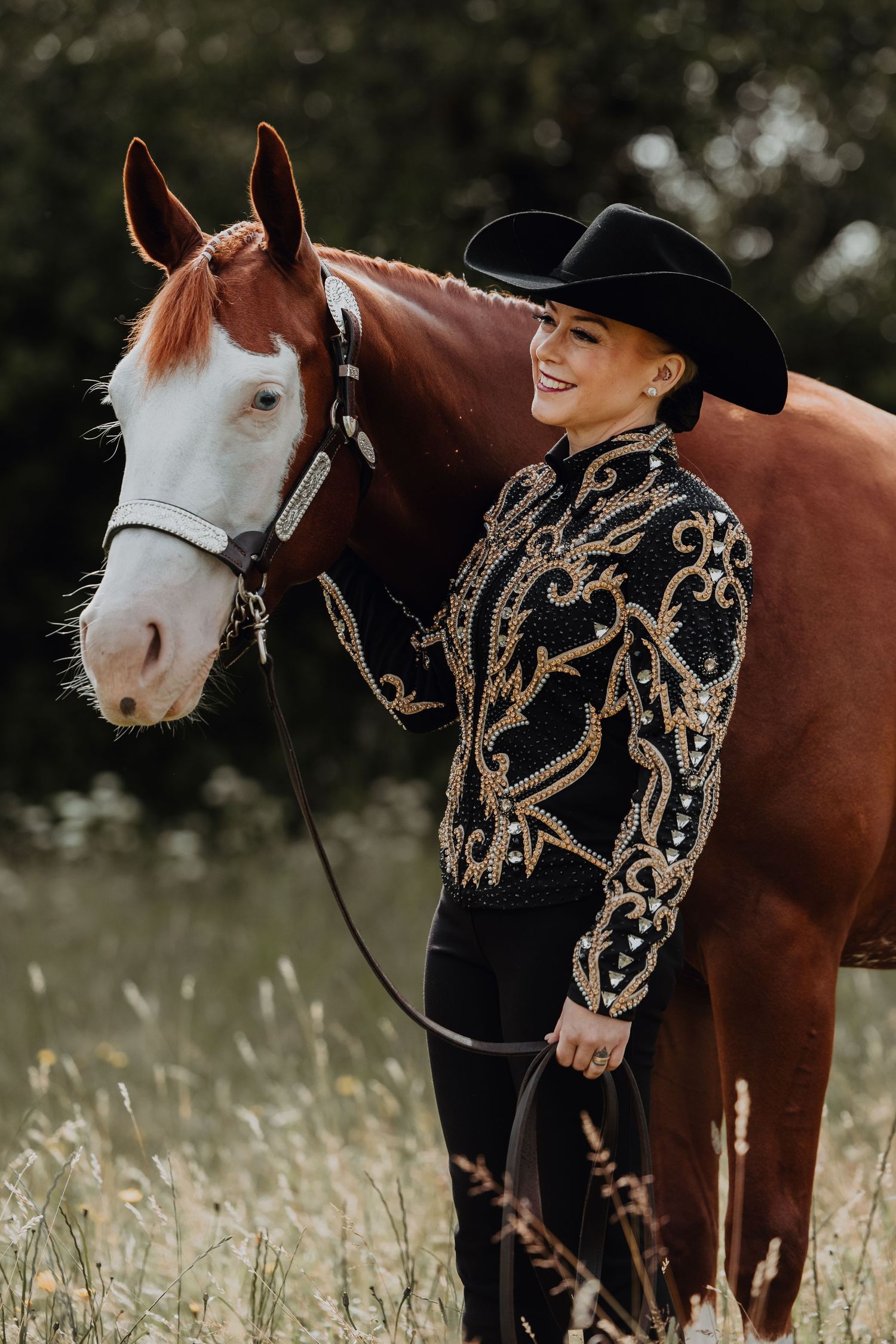 A paint horse poses with its rider wearing an ornate black and gold western show outfit.