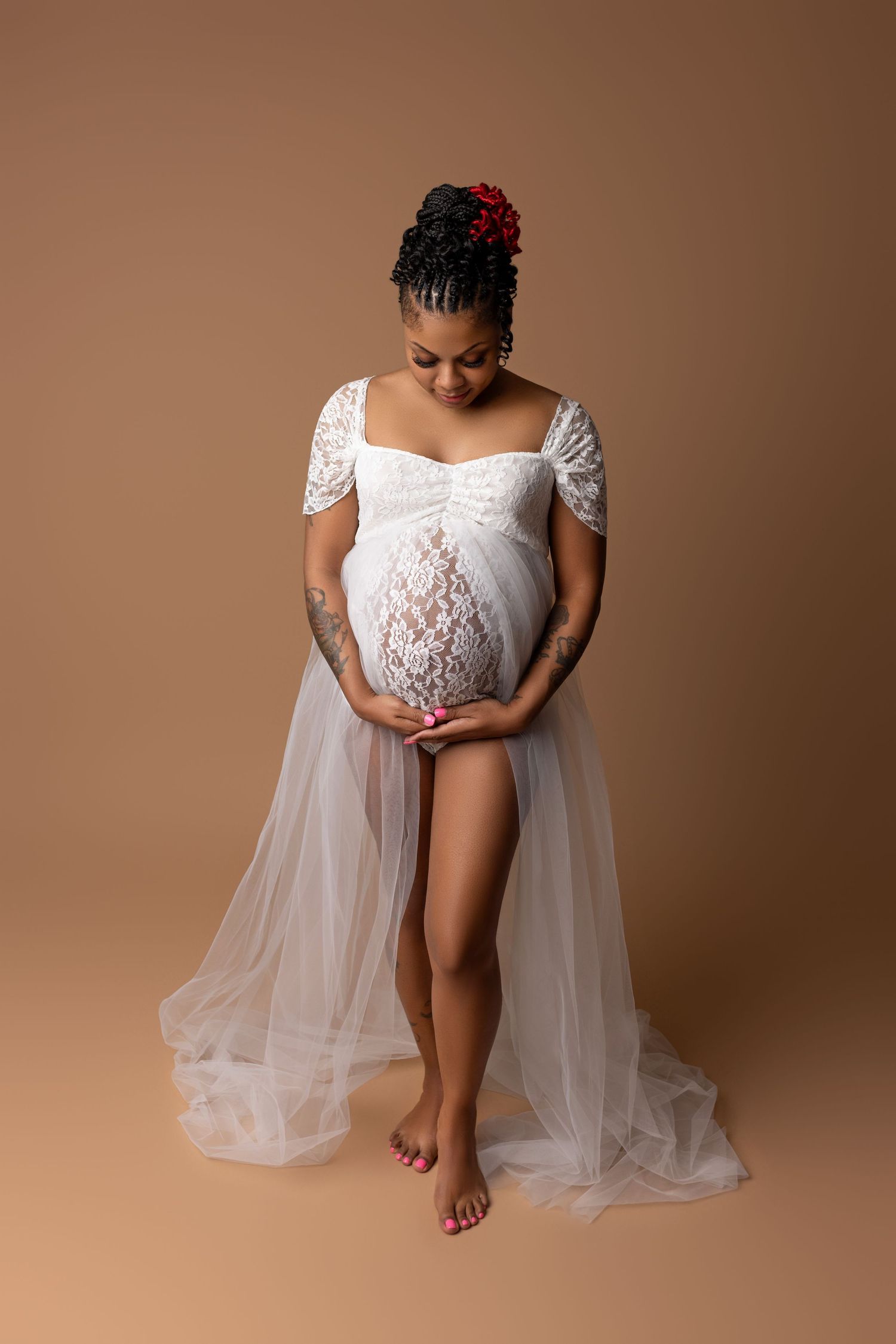 Pregnant woman in a white tulle and lace dress, holding her belly, in Cedar Park, TX maternity studo