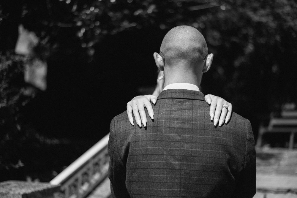 Intimate black and white photo showing hands placed on groom's shoulders from behind.