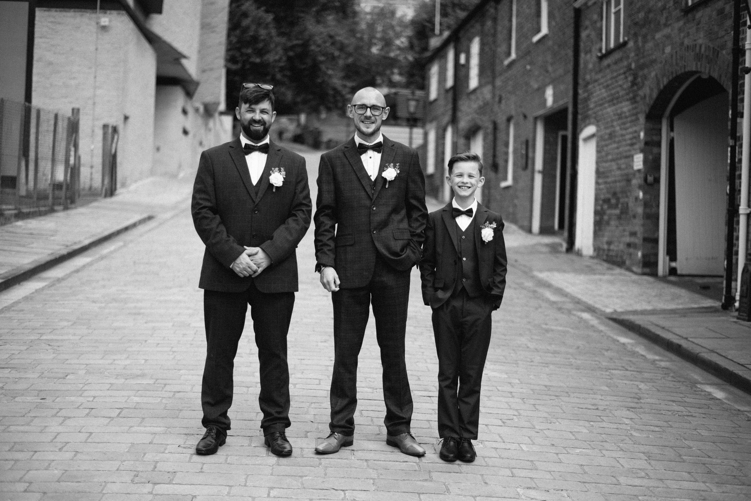 Black and white photo of three formally dressed people standing on a brick street.