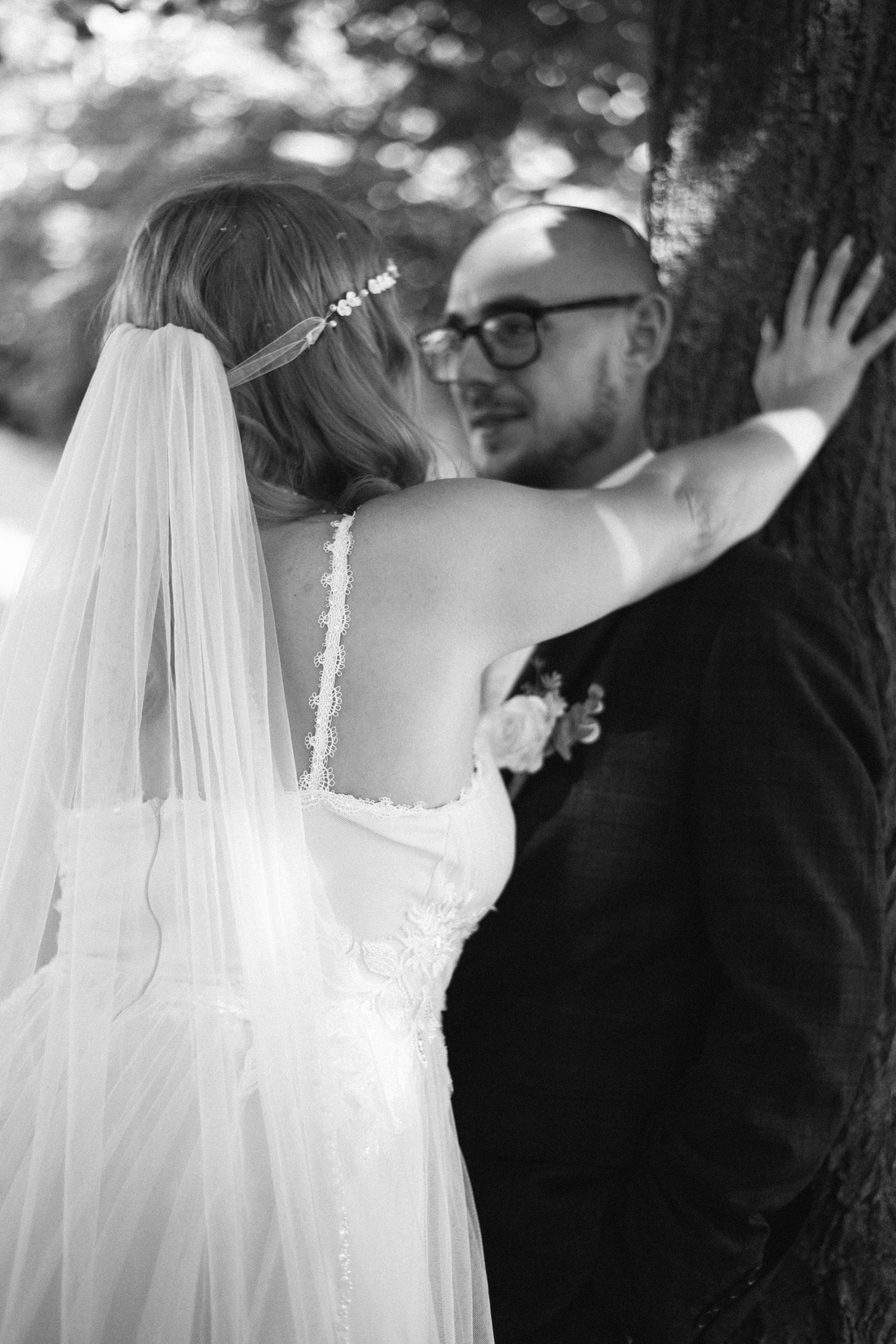 Romantic black and white photo of couple embracing against tree trunk.
