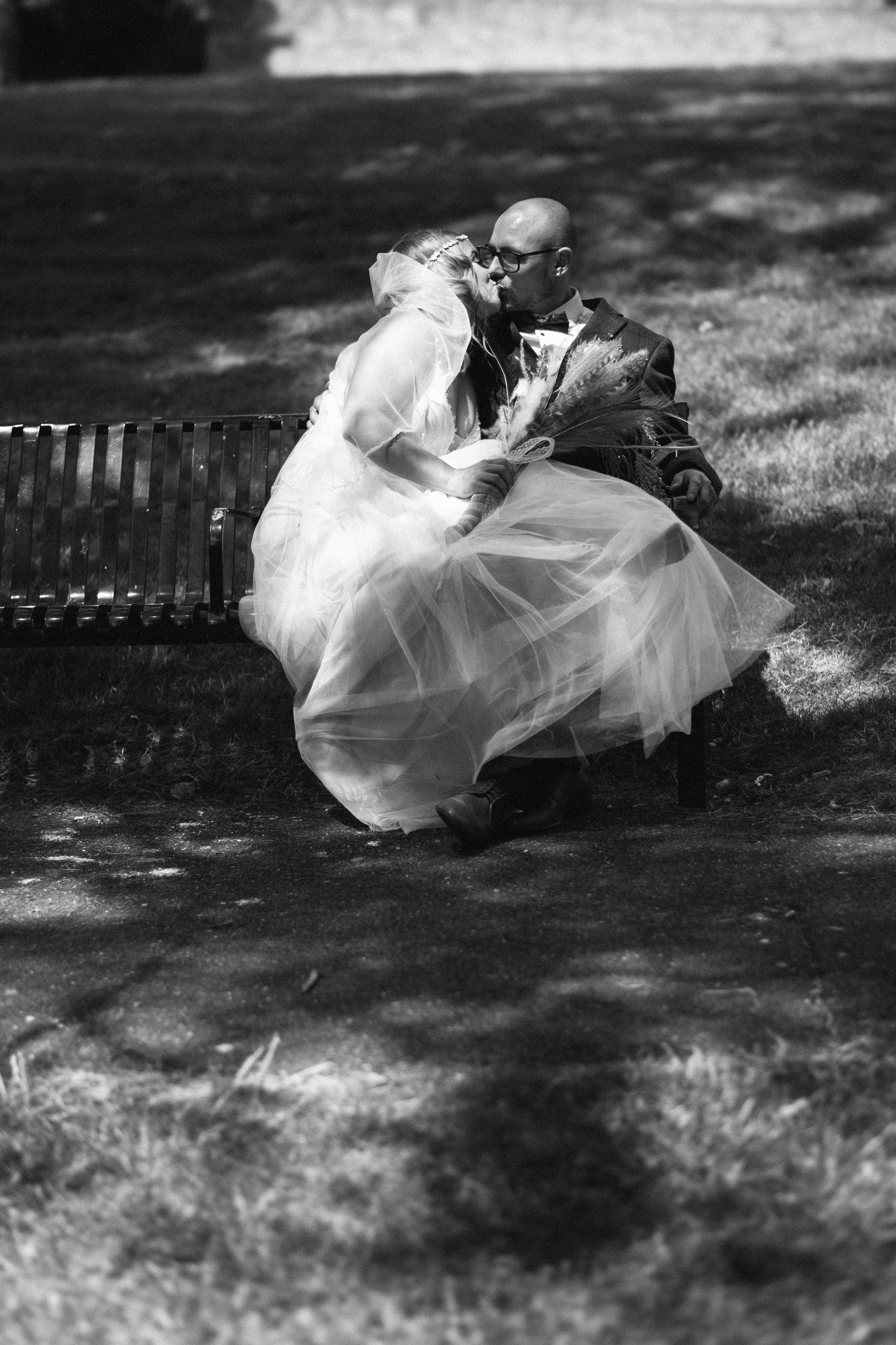 Artistic black and white shot of couple sharing intimate moment on park bench.