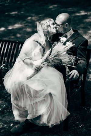 Romantic black and white photo of couple on park bench with flowing wedding dress.