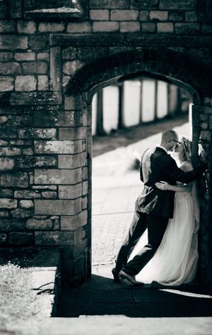 Artistic wedding photo of couple embracing under stone archway.