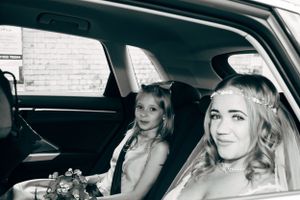 Black and white photo of two women sitting in car backseat during wedding celebration.