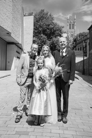 A formal wedding group photo with a church spire visible in the background.