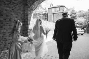 A wedding party walks along a brick path outside a church on a sunny day.