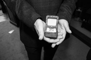 Hands hold an engagement ring box showcasing a diamond ring in black and white photography.