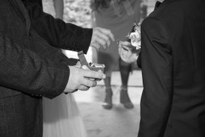 Close-up black and white shot of hands exchanging wedding rings during a ceremony.