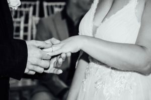 Black and white close-up of hands during a wedding ring exchange ceremony.