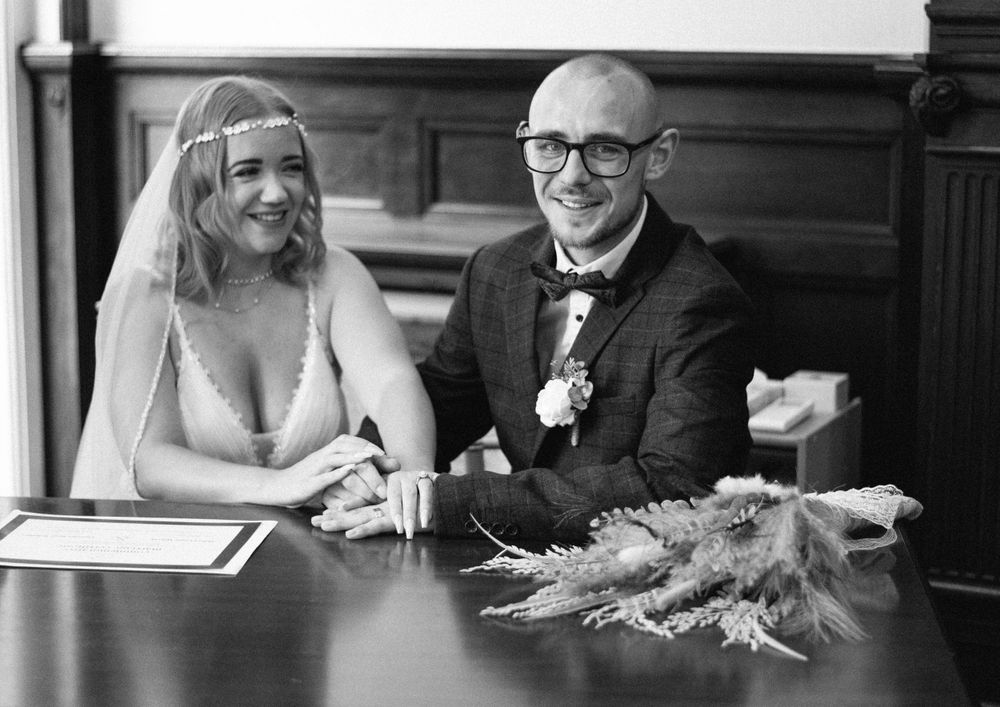 Black and white photo of a bride and groom signing documents at a formal ceremony.