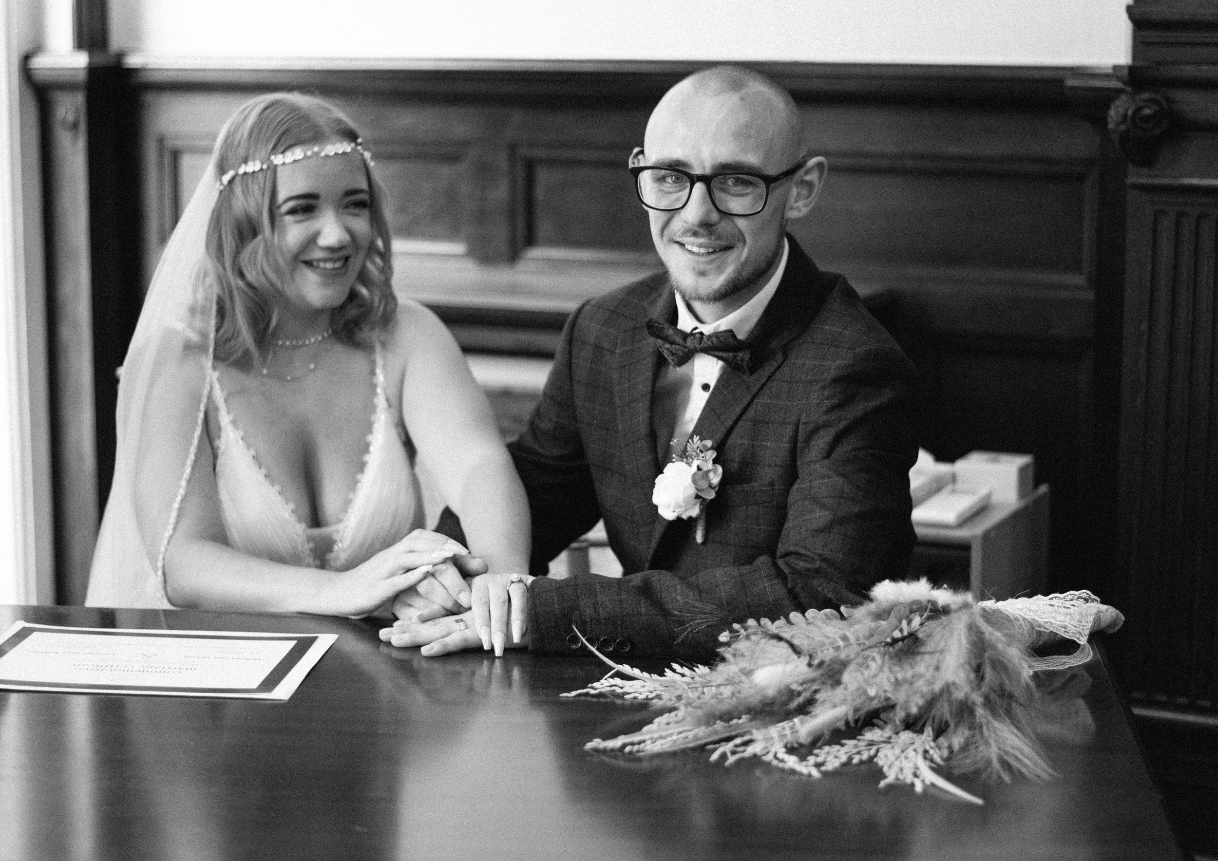 Black and white photo of a bride and groom signing documents at a formal ceremony.