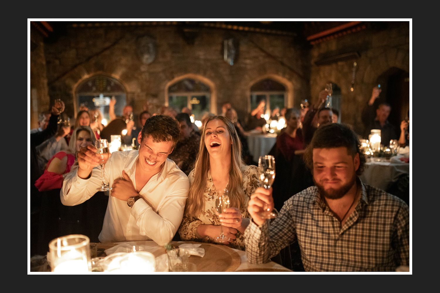 Lively wedding reception scene with guests laughing and celebrating at a candlelit table.