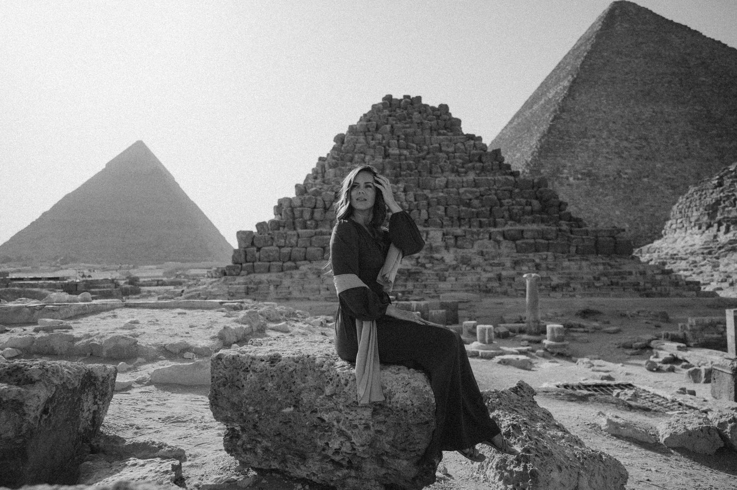 Black and white photograph of a visitor sitting on ancient ruins at the Giza pyramid complex.
