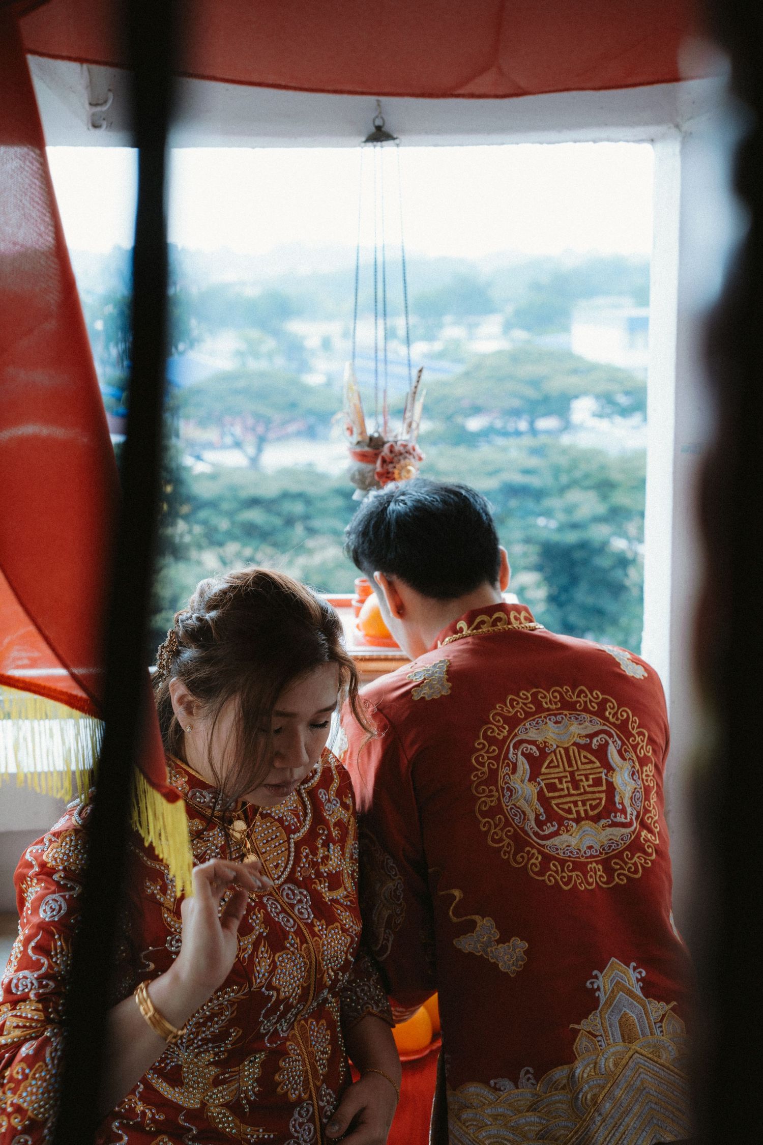 Two people in red traditional Chinese outfits looking out a window with a scenic view.