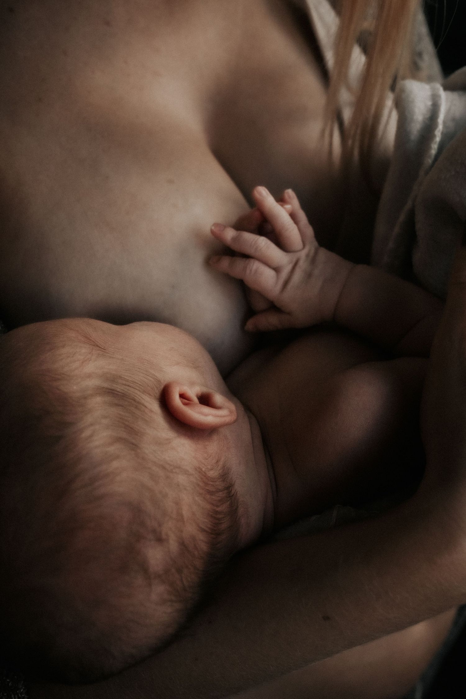A tender moment captured of an infant breastfeeding in dim lighting, showing the natural bond between mother and baby.