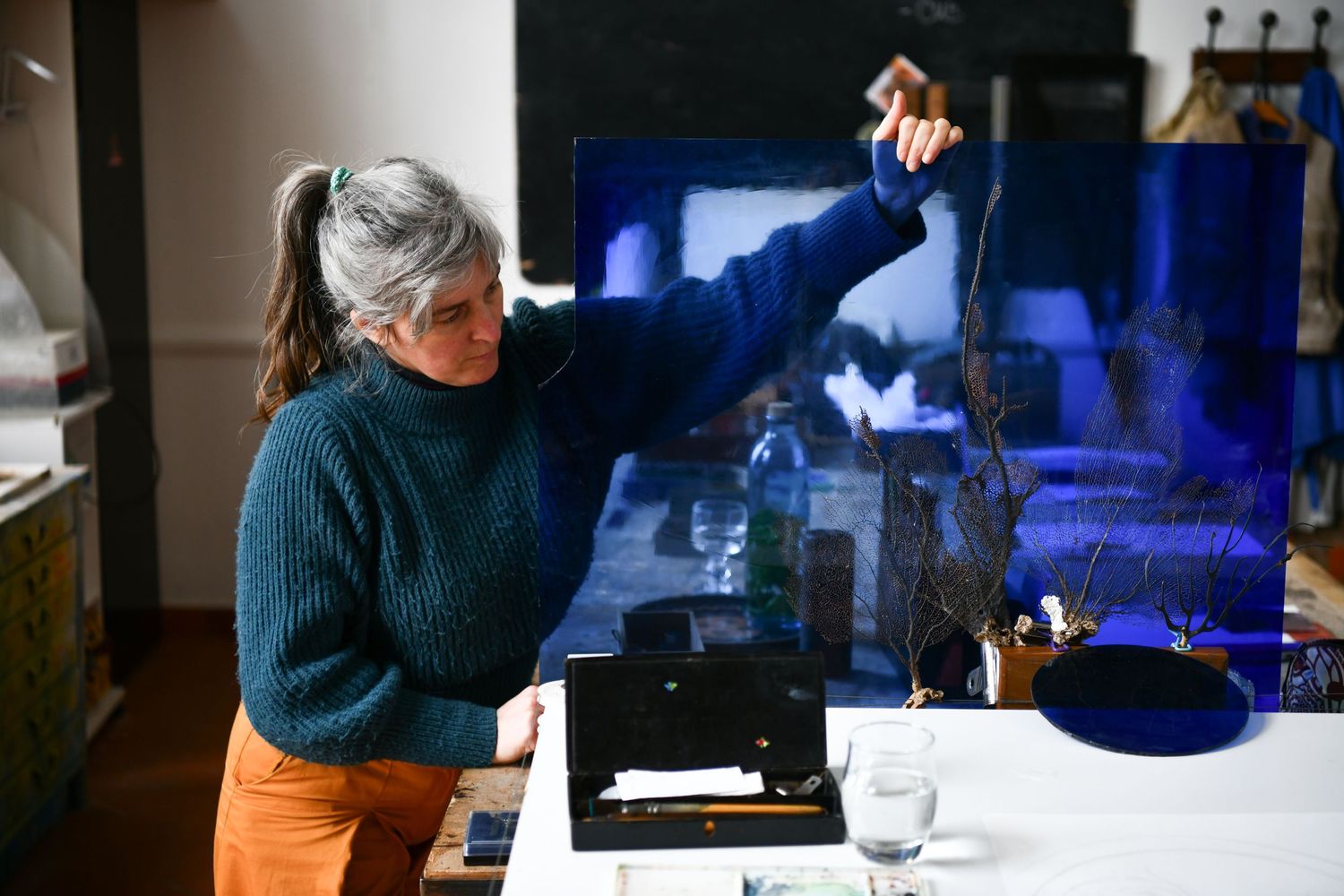 chloe quiban tenant une feuille de verre teintée bleur, portrait d'atelier par Anne-Pierre Gaignon