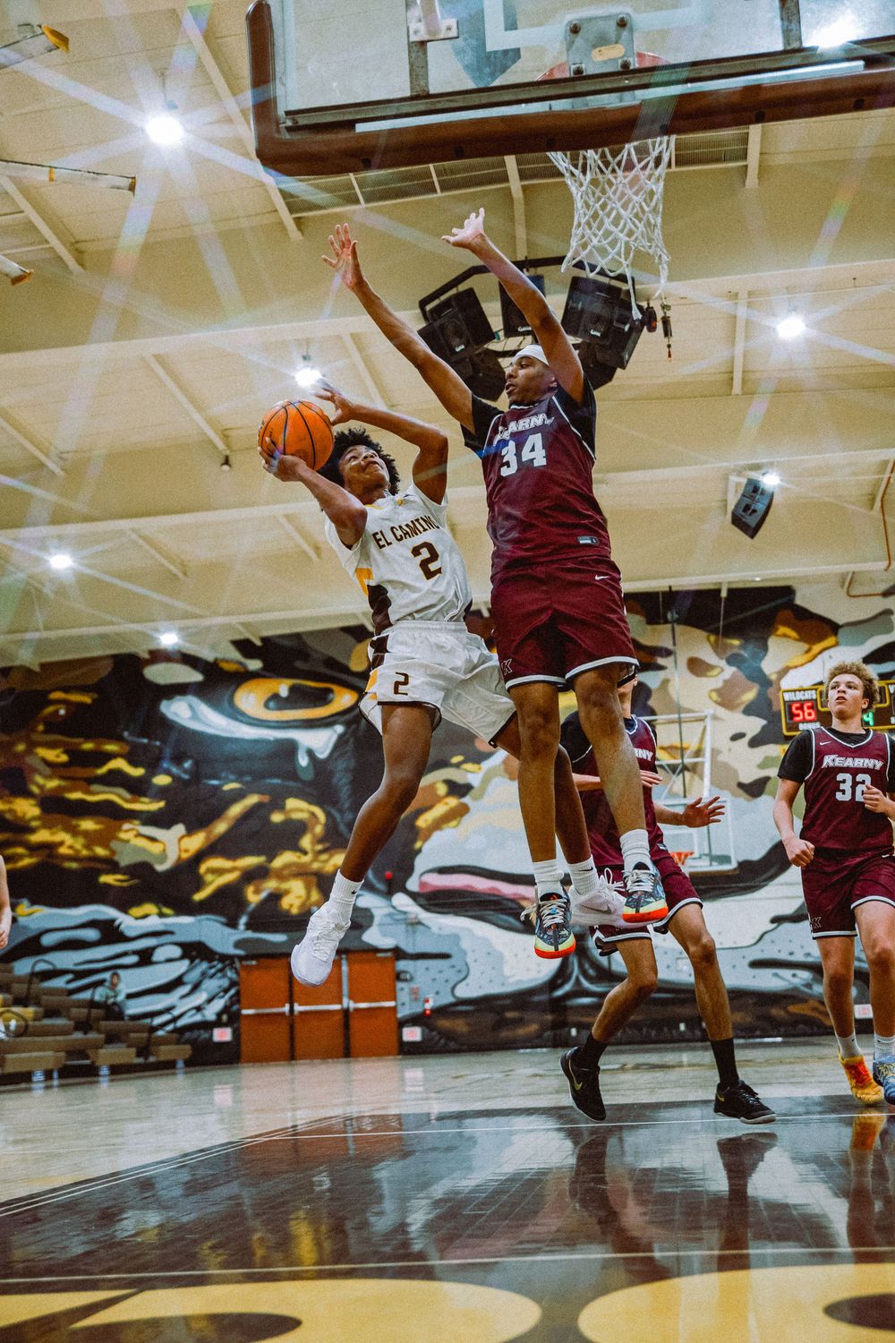 Two basketball players leap high in the air during an intense game, with one attempting a shot while the other defends.