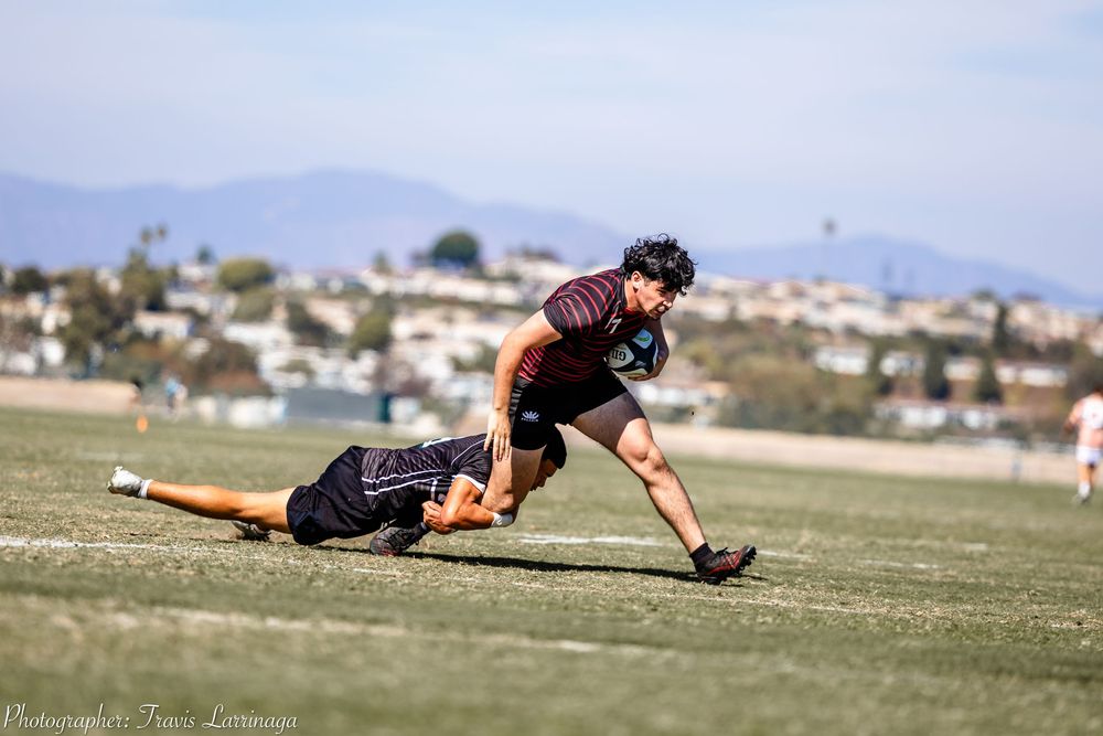 Players diving and sliding across a grass field during a rugby match.