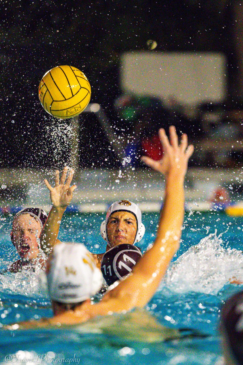 Water polo players battling for possession of the yellow ball during a competitive match.
