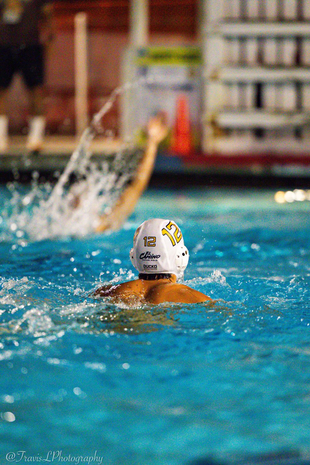 Athletes competing in a water polo match with splashing water and white caps.