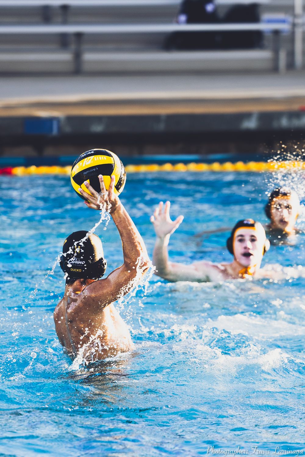 Water polo players reaching for a yellow ball during an intense match in a pool.