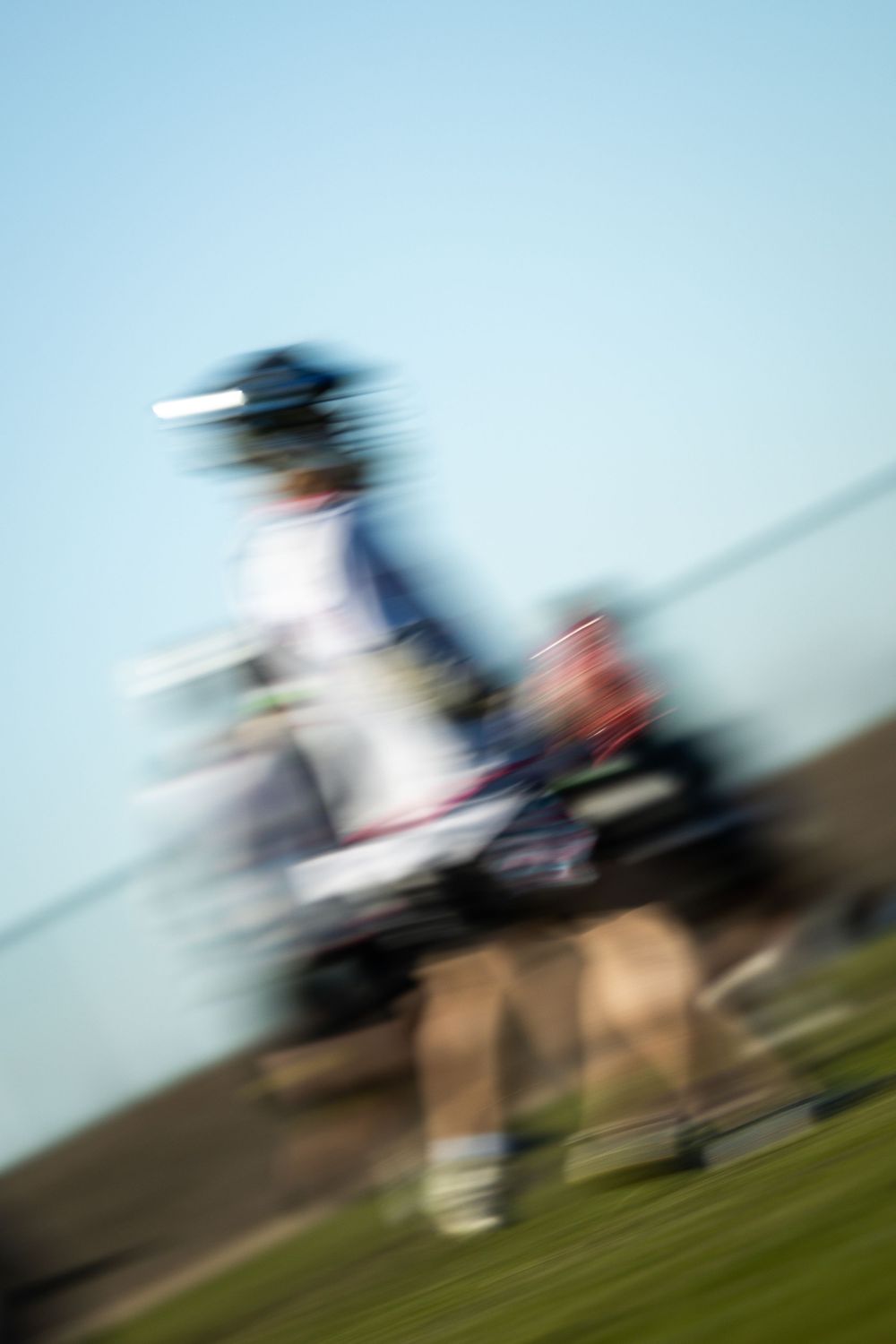 Motion blurred sequence of horse riders galloping across a grassy field on a sunny day.