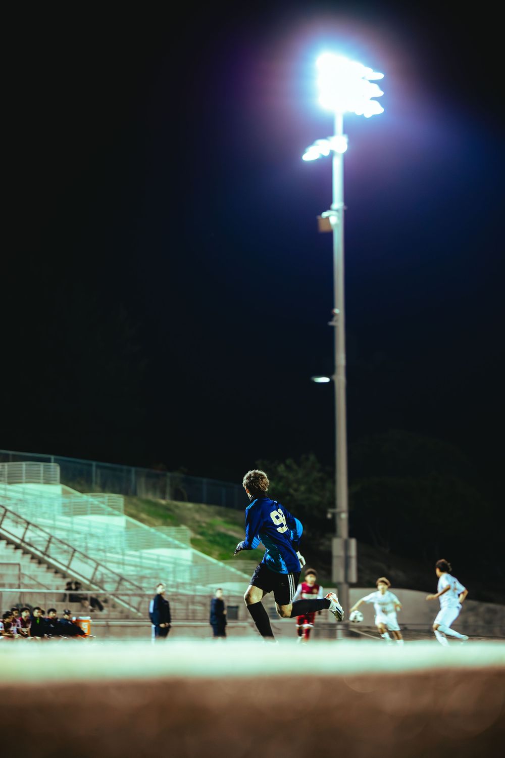 Soccer players compete under bright stadium lights on a field during a nighttime match.