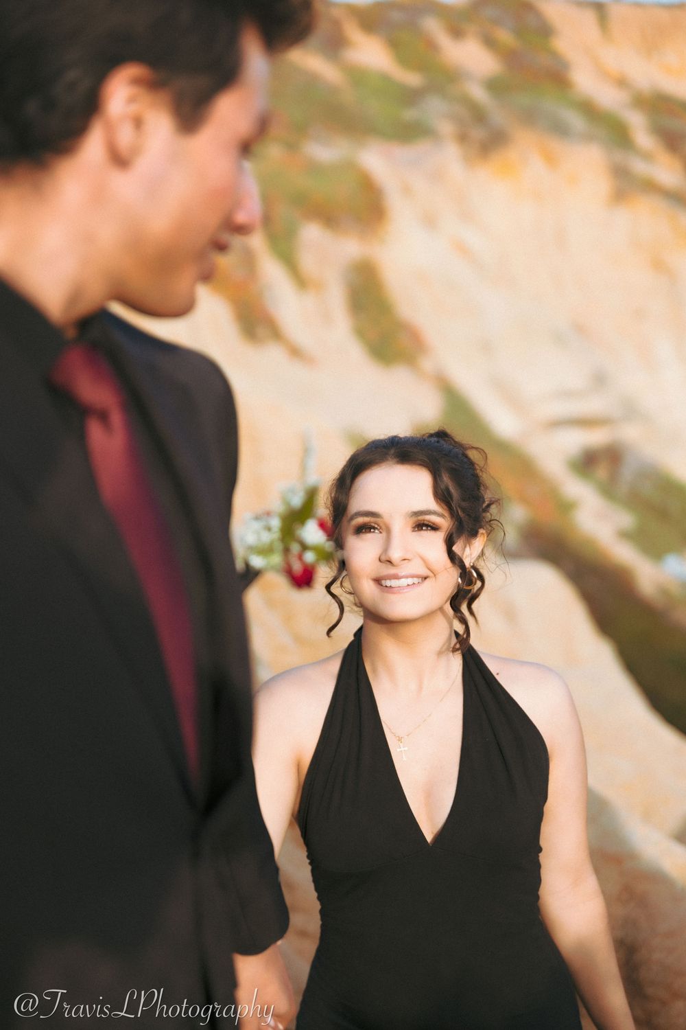 Couple in formal attire sharing a romantic moment against coastal cliffs.