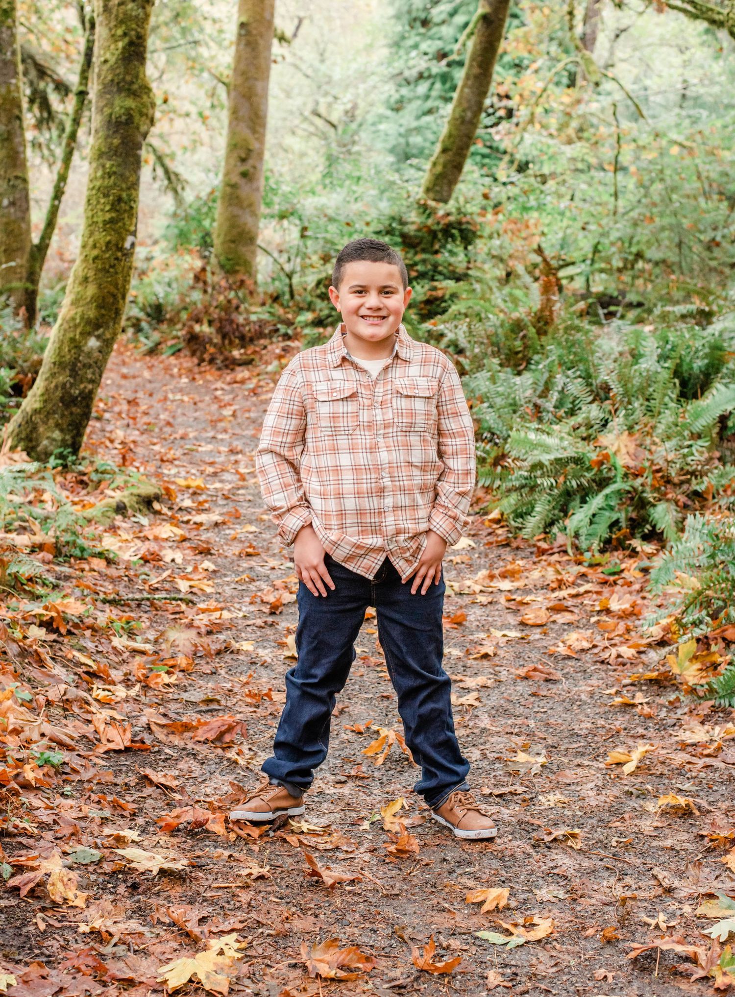 A casual outdoor portrait on a forest trail covered in fallen autumn leaves.