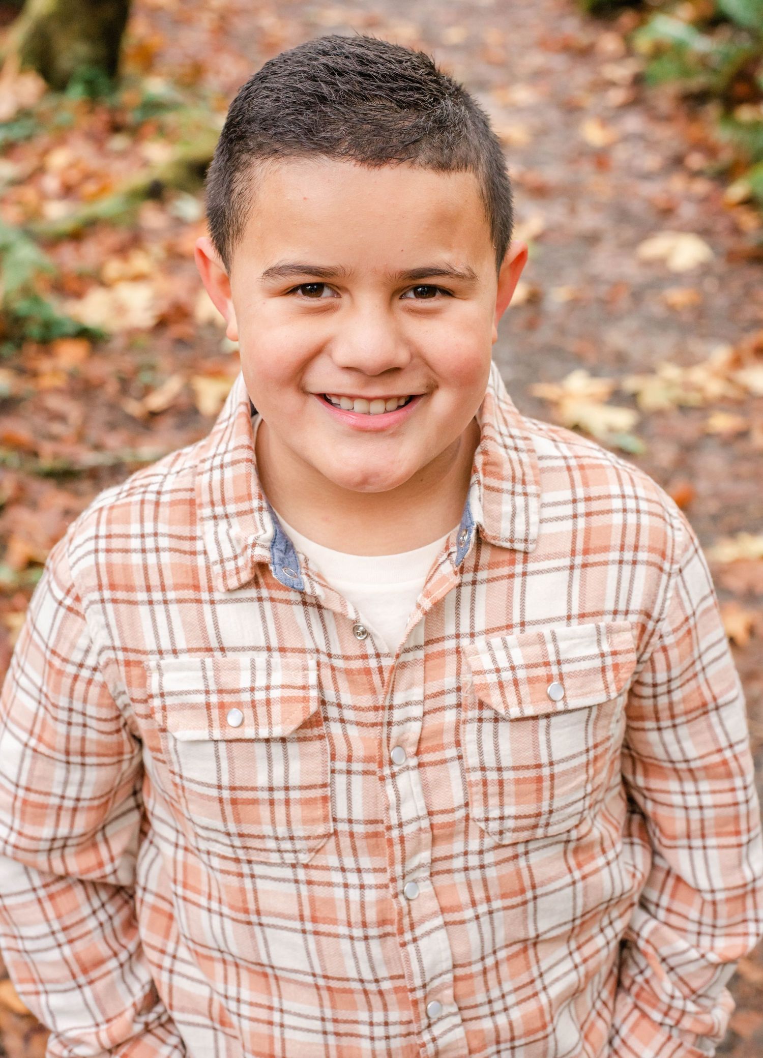 An outdoor portrait in a plaid shirt against a wooded autumn background.
