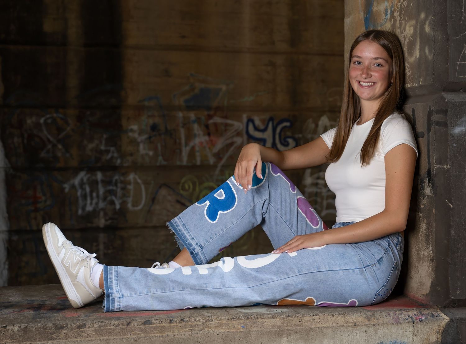 Casual portrait session on concrete ledge wearing white top and jeans.