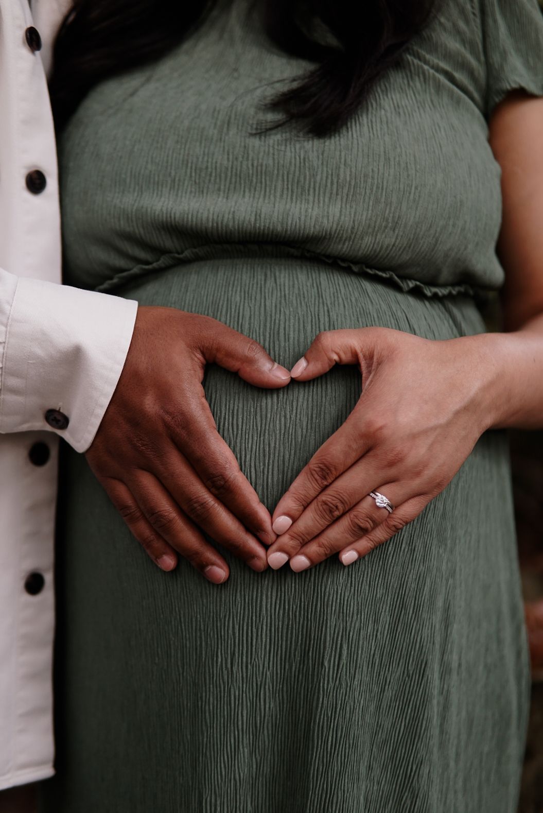 Two hands forming a heart over a baby bump