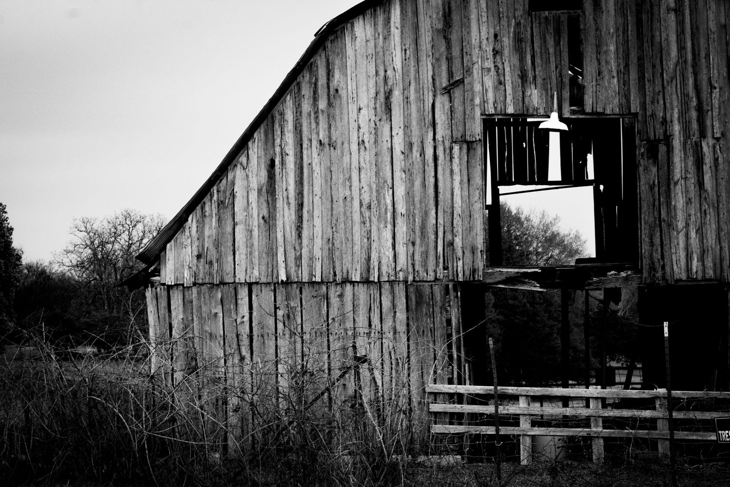 Black and white photograph of weathered wooden barn with small window opening.