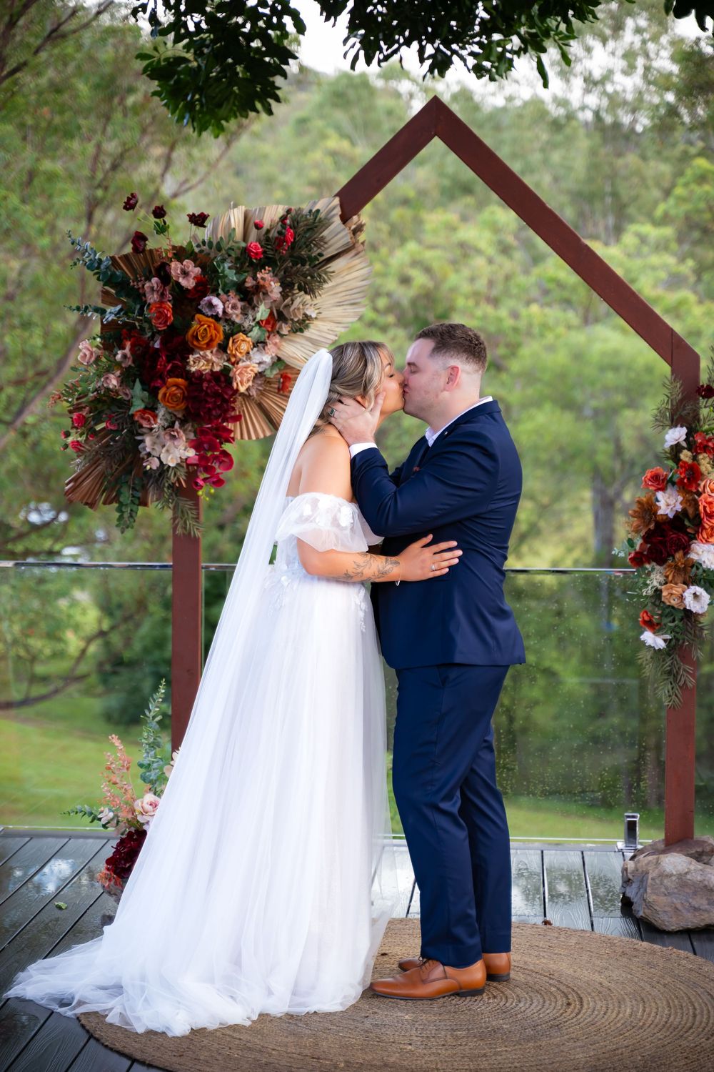 Wedding ceremony under a wooden arbor decorated with dramatic red and white floral arrangements.