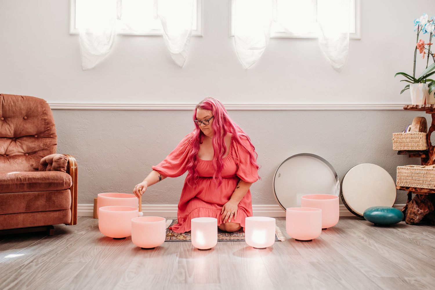 Person in pink dress arranging glowing crystal singing bowls on wooden floor.