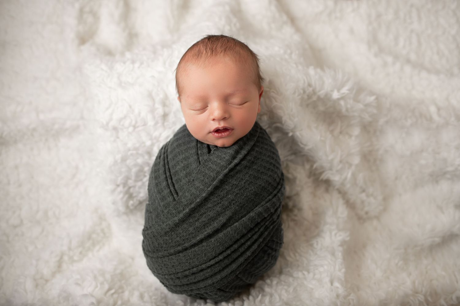 Peaceful sleeping newborn wrapped in gray swaddle on white textured background.