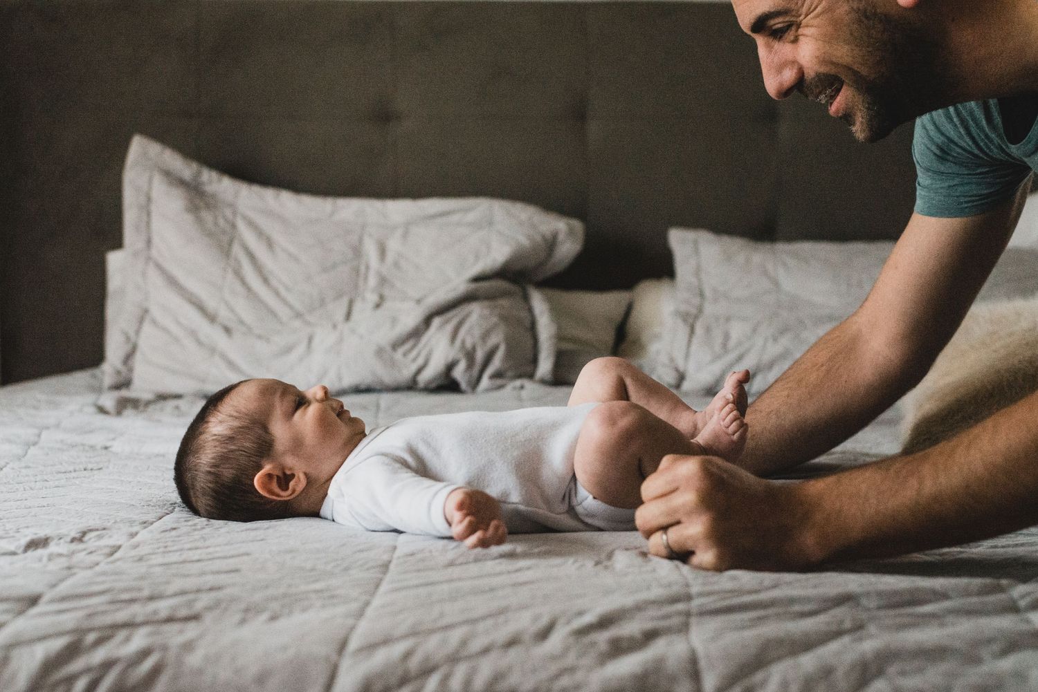 bebé recién nacido sobre la cama, su papá se reclina sobre el , se miran y ríen