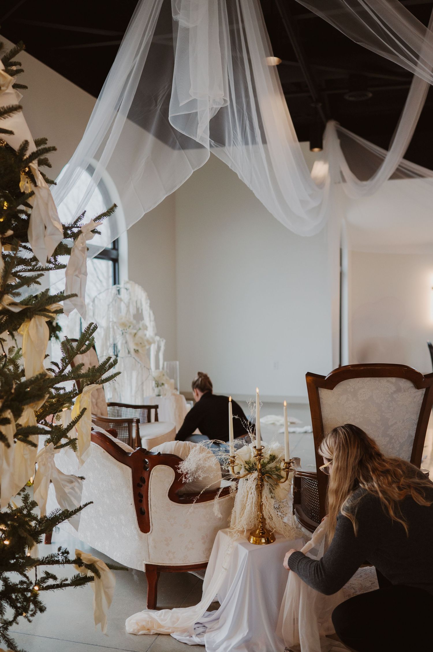 Elegant winter wedding setup with draped white fabric, candlelight, vintage chairs and decorated Christmas tree.
